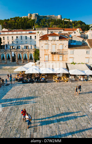 Touristen in St. Stephens Platz, mit der spanischen Festung (Fortica) oberhalb der Stadt Hvar, Insel Hvar, Dalmatien, Kroatien Stockfoto