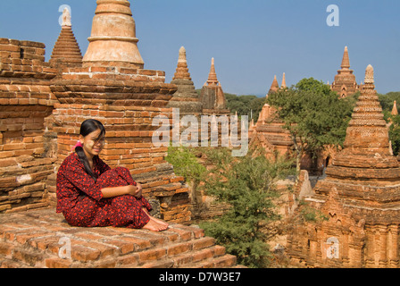 Junge burmesische Frau in einem roten Kleid sitzt auf dem Dach eines Tempels, Bagan (Pagan), Birma Stockfoto