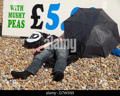 An einem heißen Tag ein Mann schläft im Schatten von seinen Regenschirm, auf Brighton Beach Stockfoto