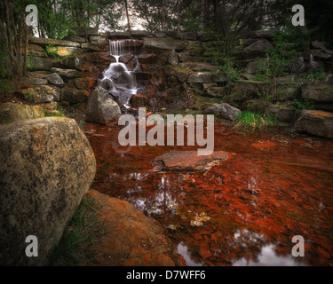 Ein kleiner Wasserfall Kaskaden über moosige Felsen in einer schönen steinernen Grotte. Stockfoto