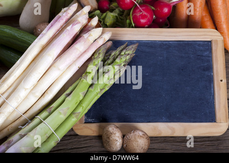 Grünen und weißen Spargel sind zusammen mit Gemüse der Saison und ein Schiefer auf einem hölzernen Hintergrund Stockfoto