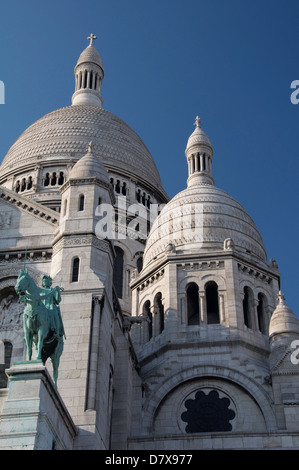 Die hoch aufragenden weißen Kuppeln der Basilika Sacré-Coeur auf dem Montmartre. Über dem Portikus steht ein Reiterstandbild der Jeanne d ' Arc. Paris, Frankreich. Stockfoto