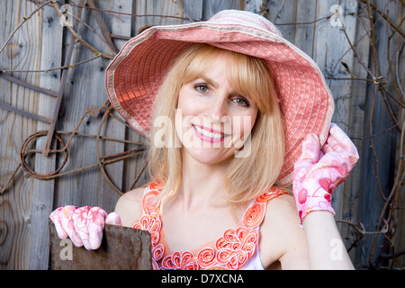 Attraktive Frau mit Gartenarbeit Mütze und Handschuhe posiert vor der alten Zaun Stockfoto