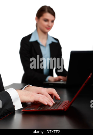 Männerhände auf einem roten Notebook vor einer jungen Frau mit einem Laptop auf einem schwarzen Tisch in einem Büro arbeiten. Stockfoto