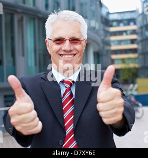 Glücklich senior Business-Mann hält seine Daumen außerhalb des Büros Stockfoto