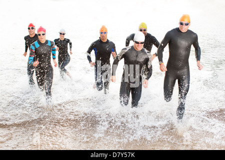 Triathleten in Neoprenanzüge in Wellen laufen Stockfoto