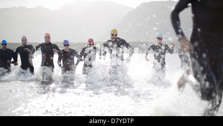 Triathleten in Neoprenanzüge in Wellen laufen Stockfoto