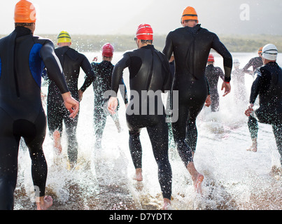 Triathleten in Neoprenanzüge in Wellen laufen Stockfoto