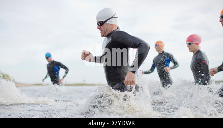 Triathleten in Neoprenanzüge in Wellen laufen Stockfoto