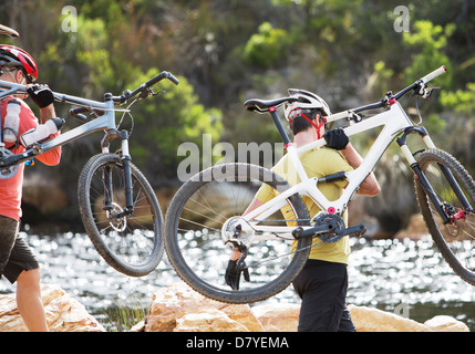 Männer tragen Mountainbikes im Fluss Stockfoto