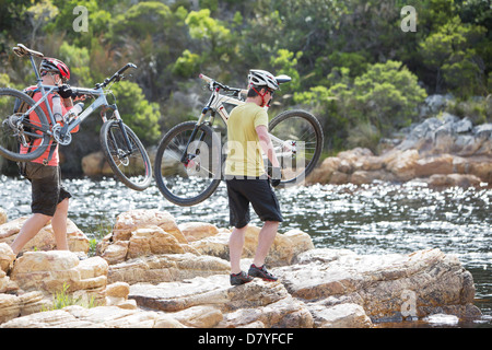 Männer tragen Mountainbikes auf Felsformation Stockfoto