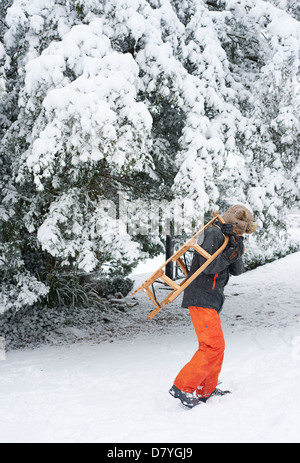 Jungen tragen Holzschlitten im Schnee Stockfoto