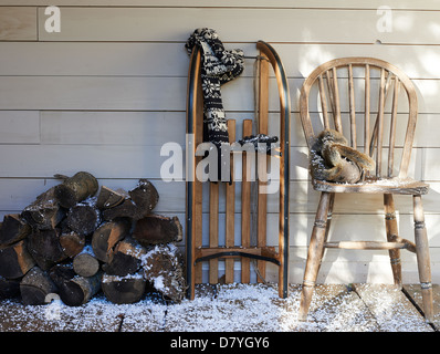 Schal, Holzschlitten, Stuhl und Brennholz auf Veranda Stockfoto