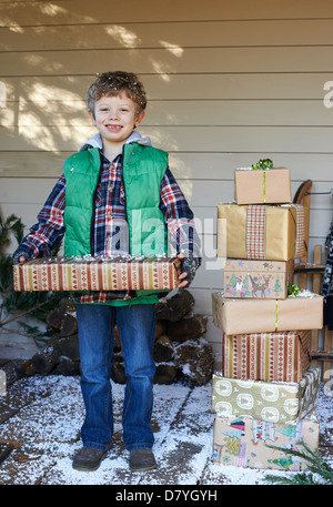 Junge hält Weihnachtsgeschenke auf verschneiten Veranda Stockfoto