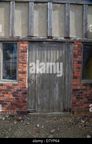 Alte Holztür in heruntergekommenen kleinen halben Holzhaus in rotem Backstein Stockfoto