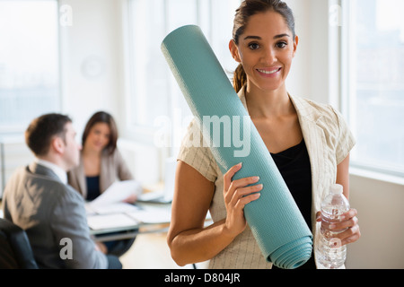 Geschäftsfrau hält Yoga-Matte im Büro Stockfoto