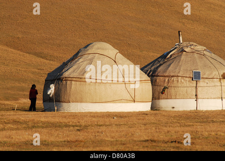 Eine Mädchen steht in der Nähe von zwei kirgisischen Jurten bei Sonnenuntergang in der Hochland-Weiden am Song-Kul-See. Naryn Region, Kirgisistan Stockfoto