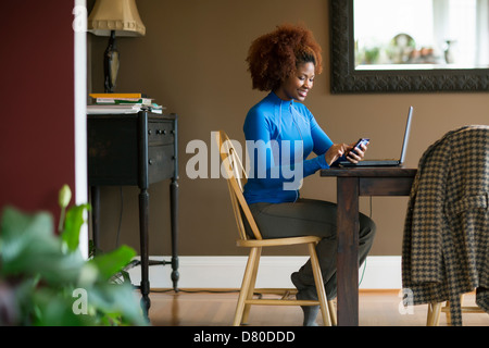 Schwarze Frau mit Handy am Schreibtisch Stockfoto