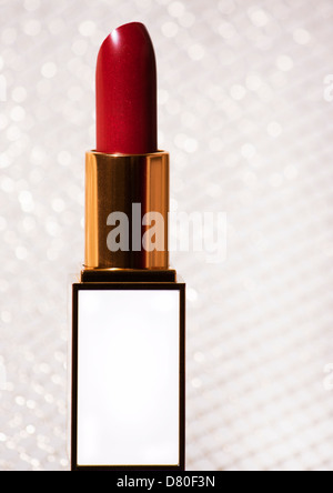 Nahaufnahme von roten Lippenstift in einem weißen und goldenen Halter vor goldenem Hintergrund Stockfoto
