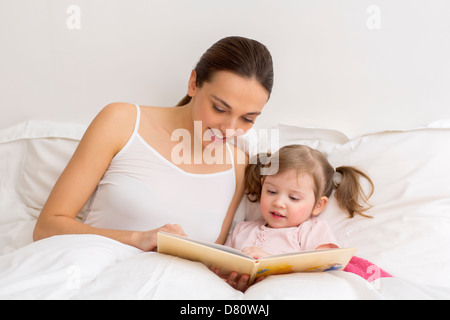 Kleines Mädchen, ein Buch zu lesen, mit ihrer Mutter in weiße Schlafzimmer Stockfoto