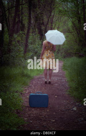 ein Mädchen mit Koffer und Regenschirm im Wald Stockfoto