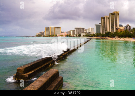 Ankommende Welle rauscht über Ufermauer am Kuhio Beach Park am Strand von Waikiki auf Oahu, Hawaii Stockfoto