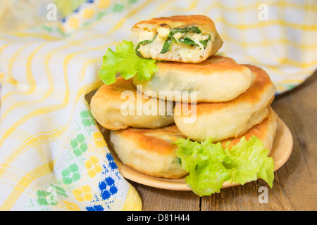 Gebratene frische leckere Bratlinge (Kuchen) gefüllt, grünen Zwiebeln und Eiern, auf Holztisch (Hintergrund). Traditionelle Frühling Fastfood. Stockfoto