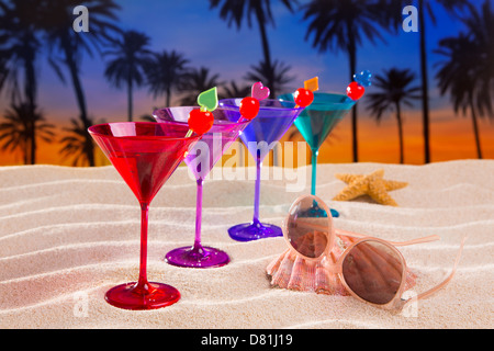 bunte Cocktails in einer Reihe mit Kirsche auf Sandstrand Palmen Bäume Sonnenuntergang Stockfoto