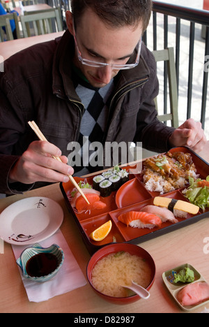 Mann in einem Straßencafé einen traditionellen Bento Box oder Sushi Lunch mit Stäbchen zu essen Stockfoto