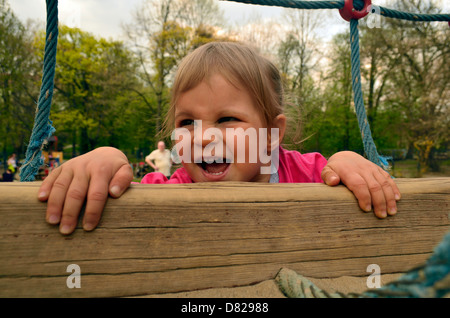 2 Jahre altes Mädchen Klettern auf Klettergerüst am Spielplatz lächelnd Stockfoto