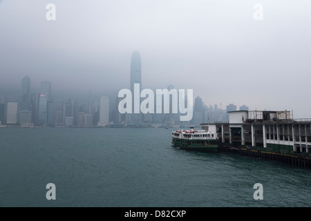 Star Ferry auf der Kowloon-Anlegestelle mit Skyline von Hong Kong Island an einem trüben Tag im Hintergrund Stockfoto