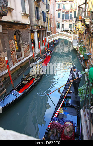 Gondeln und Gondolieri auf einer kleinen Nebenstraße Kanal mit bunten Altbauten Brücke aus Holz Liegeplatz Beiträge Venedig im winter Stockfoto