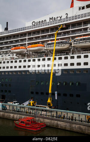 Liverpool, Vereinigtes Königreich 17. Mai 2013. Pilot Boat und Wartung Crew am Cruise Liner Terminal wo das Passagierschiff in Bermuda Liner RMS Queen Mary 2 registriert festgemacht bei ihrem Besuch in der Stadt.  Das Liverpool Cruise Terminal bei Fürsten-Parade ist eine 350 Meter lange schwimmende Struktur befindet sich auf dem Fluss Mersey ermöglichen große Kreuzfahrtschiffe, ohne in das beiliegende Dock System eindringen oder Liegeplatz Mitte des Flusses und Ausschreibung Passagiere an Land zu besuchen. Das Terminal wurde offiziell am 21. September 2007 durch seine königliche Hoheit der Herzog von Kent eröffnet, wenn die Queen Elizabeth 2 am Terminal festgemacht. Stockfoto