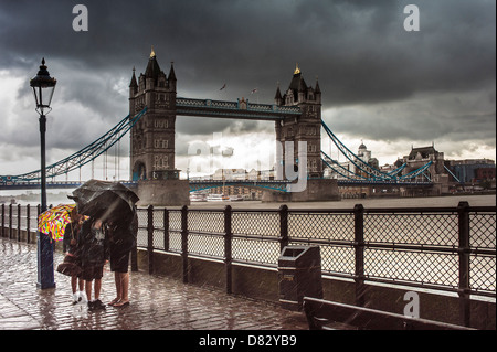 LONDON, Großbritannien - 17. JULI 2011: Schutz der Familie vor starkem Regen unter Sonnenschirmen an der Tower Bridge, London Stockfoto