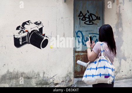 Ein Mädchen nimmt ein Foto von einer Kamera auf eine Wand in Sheung Wan, Hong Kong gemalt Stockfoto