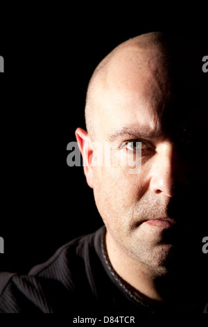 Bald leitete Mann mit Hälfte seines Gesichts im tiefen Schatten für ein dramatischer Bild direkt in die Kamera schaut. Stockfoto