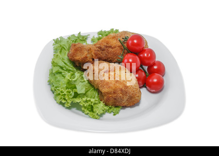 Gebratene Hähnchenstücke auf einem Teller mit Salat und Tomaten. Genommen auf einem Blatt aus weißem Kunststoff. Stockfoto