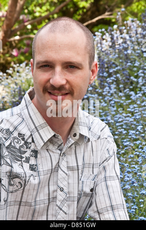 Junger kaukasischer Mann im Freien in einem Portraitkopf und Schultern geschossen. Er hat einen kahlen, rasierten Kopf, einen Ziegenbart, blaue Augen und lächelt Stockfoto