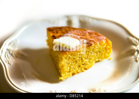 Ein Stück hausgemachtes Maisbrot auf einem weißen Teller mit weißem Hintergrund. Ein Stückchen Butter schmelzen an der Spitze. Oklahoma, USA. Stockfoto