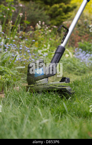 Strimming lange Grashalme gegen eine Blume-Grenze in einem englischen Garten Stockfoto