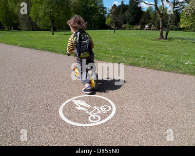 Ein 3 Jahre alter Junge mit Rucksack, sein Fahrrad durch ein Fahrrad Logo auf dem Radweg in Bute Park im Frühling, Cardiff Wales UK KATHY DEWITT Stockfoto