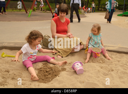 2 und 4 Jahre alte Mädchen mit Mutter in Sand Grube spielen Spielzeug Spielplatz Stockfoto