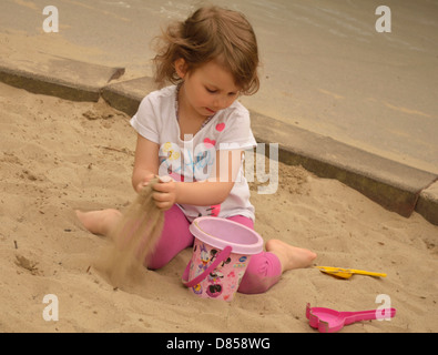 Kleine Mädchen spielen im Sand am Spielplatz Füllung Eimer mit sand Stockfoto