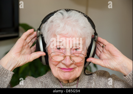 Eine ältere Frau, die äußere Ohr Kopfhörer tragen Stockfoto