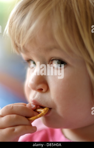 Kleines Mädchen Kind beißen Brezel mit Blickkontakt Stockfoto