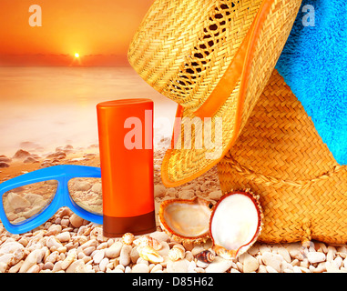 Closeup Strandzubehör auf Sonnenuntergang auf der steinigen Küste, Hygiene Zubehör, Schnorchel Maske, Sonnencreme, Hut, Tasche und Handtuch Stockfoto