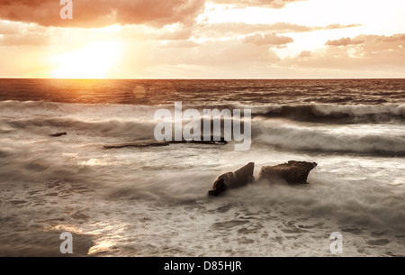Schöne orange Sonnenuntergang über stürmische See, felsigen Küste, tropischen Strand im Abend, dramatische Landschaft, bewölkten Wetter Stockfoto