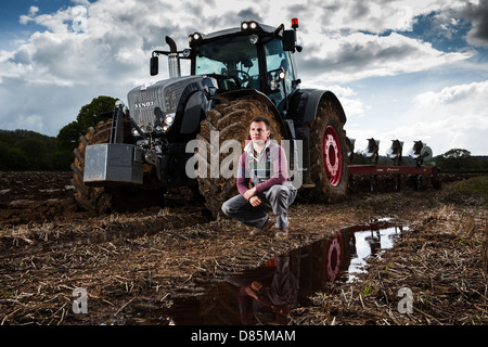 Porträt eines jungen Landwirts mit Traktor und Pflug in einem Acker. Stockfoto