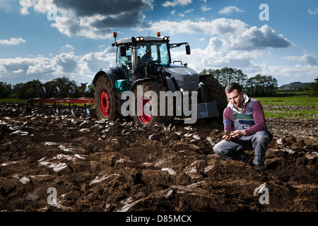 Porträt eines jungen Landwirts mit Traktor und Pflug in einem Acker. Stockfoto