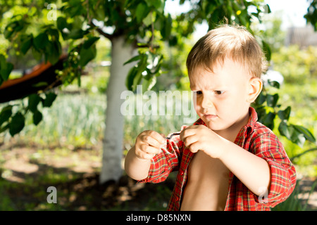 Kleiner Junge mit einem verwirrten Ausdruck Holding Regenwurm in seinen Händen, die er aufmerksam studiert, steht er im Garten Stockfoto